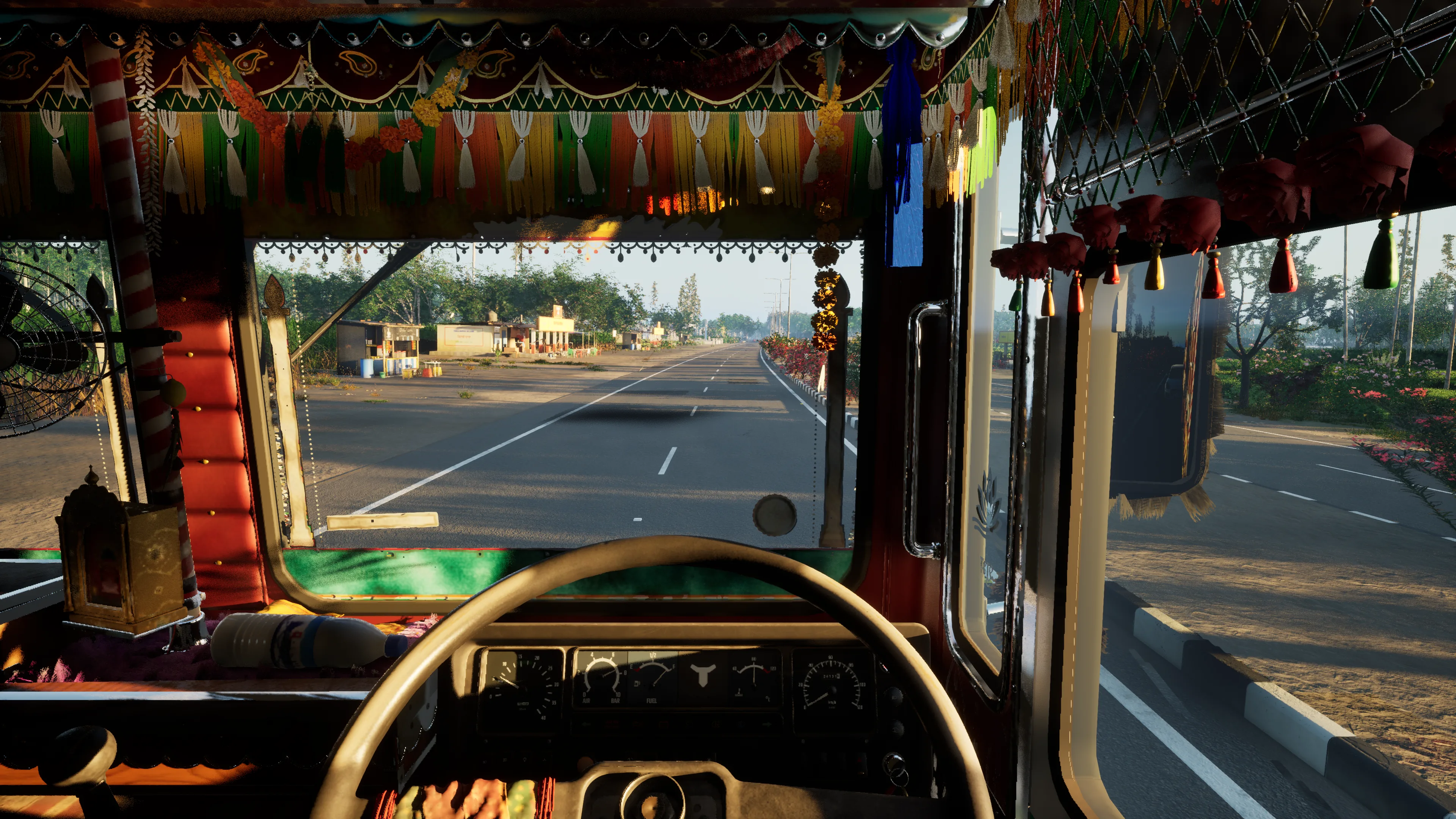 The driver’s view from the cab: a decorated dash with a small shrine, tassels and marigolds across the windscreen, and a straight highway ahead