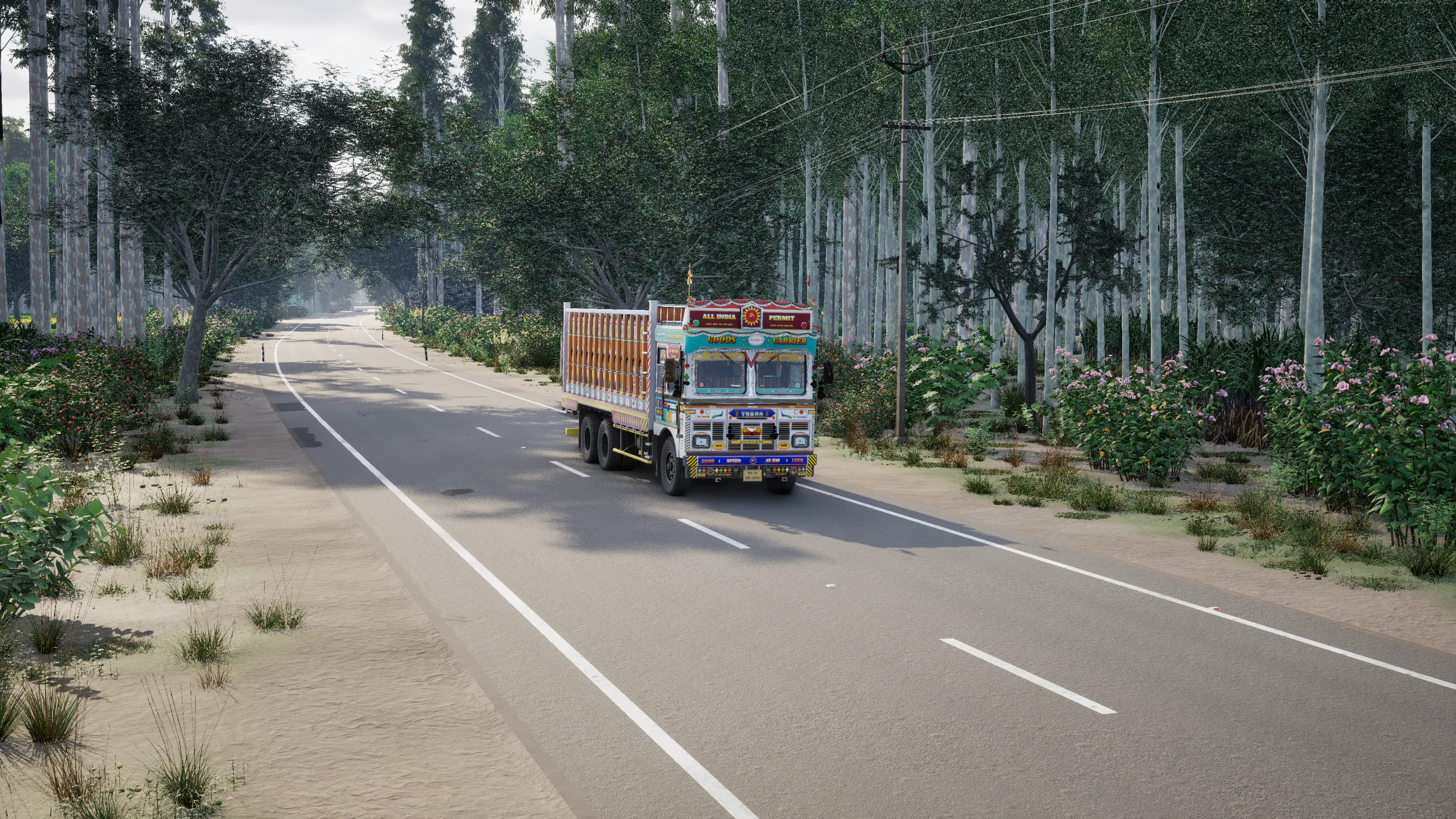A painted truck on a two-lane road lined with tall trees and flowering shrubs, in bright morning light