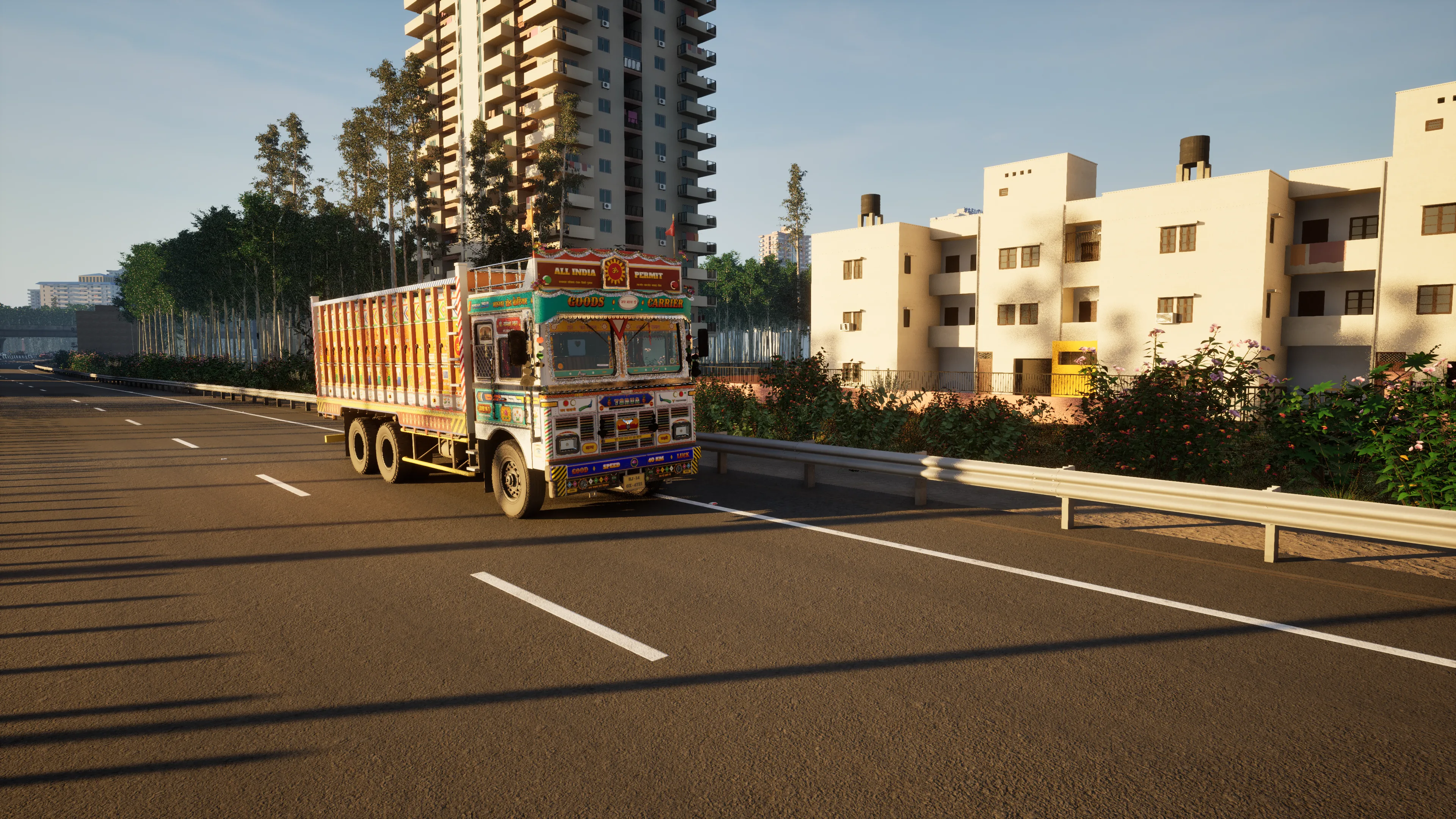 A painted truck on an empty multi-lane road in low evening sun, a residential tower and cream low-rise flats behind a guardrail