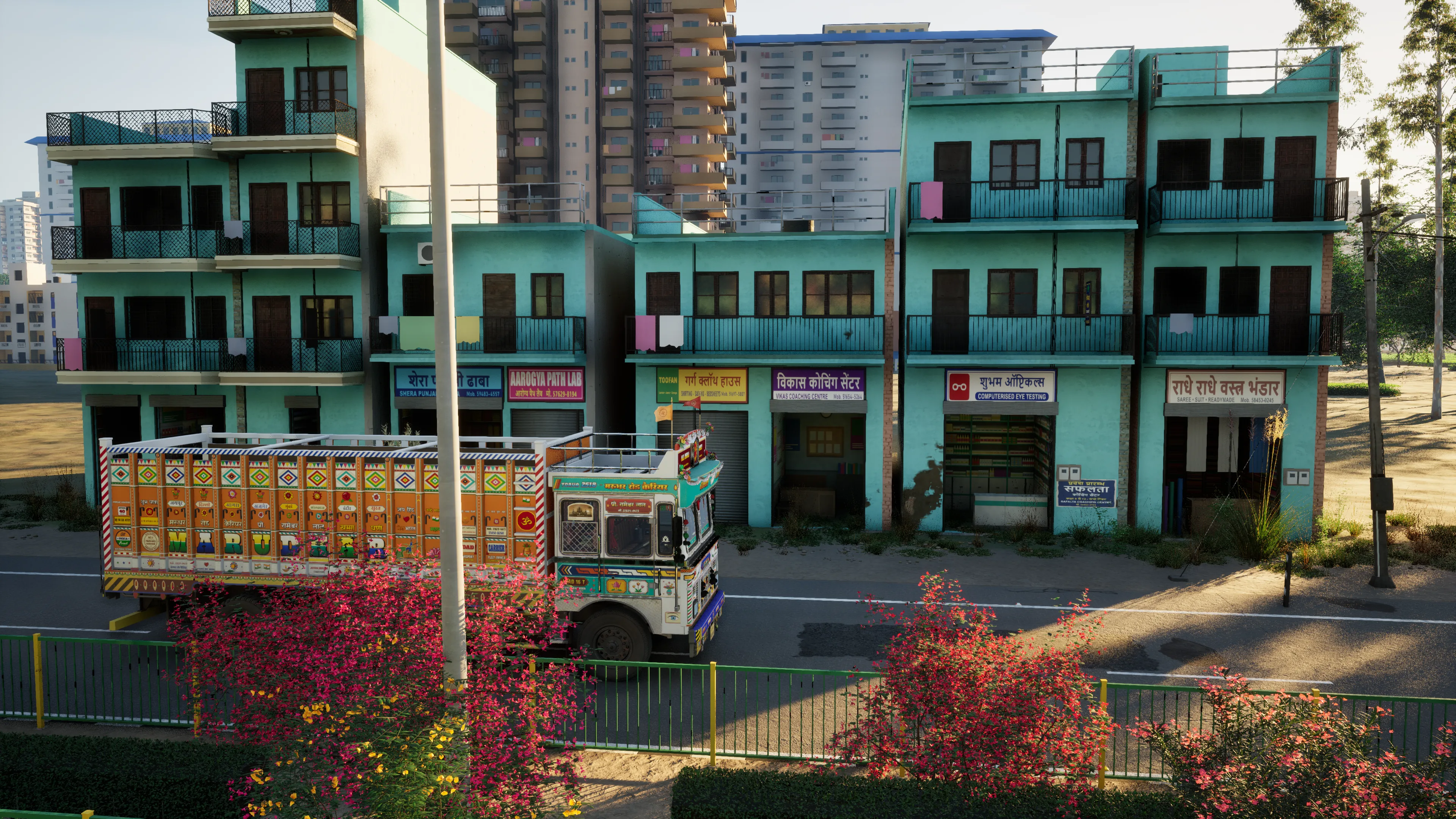 A painted truck passing a row of turquoise shop-houses with Hindi and English signboards, pink bougainvillea in front and apartment towers behind