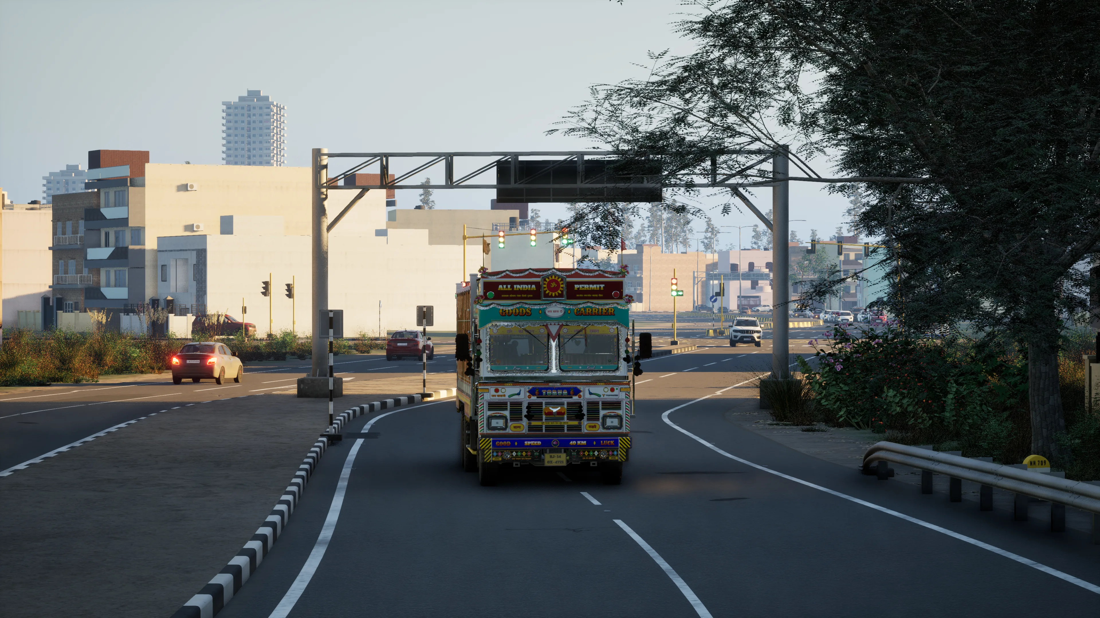 A painted truck on a town road just past an overhead gantry, traffic lights and cars at the junction behind it