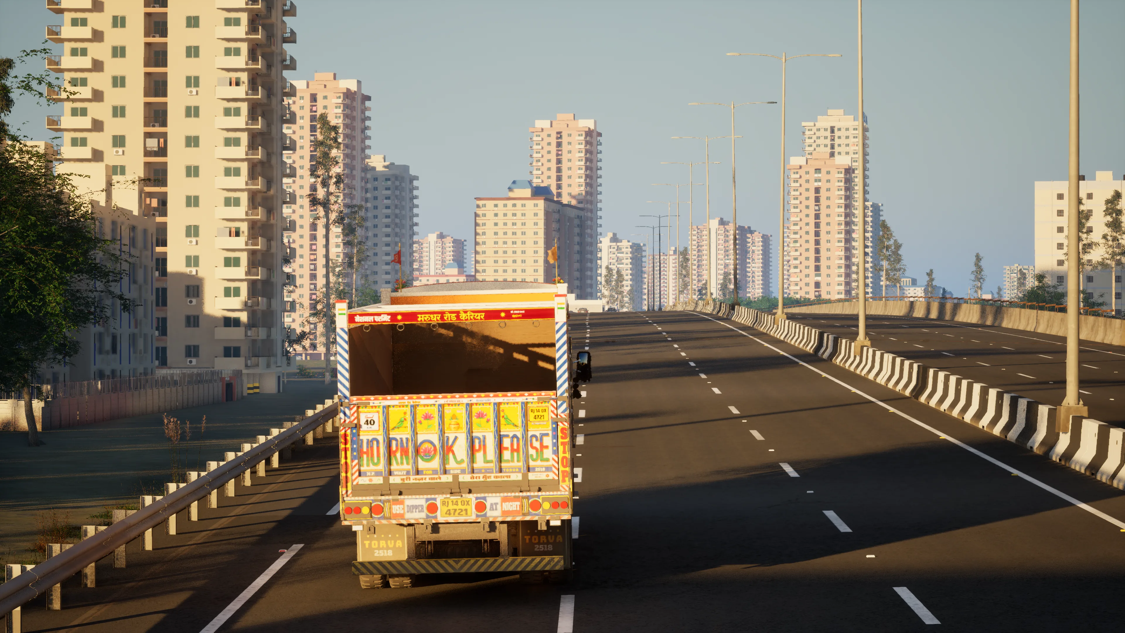 The back of the truck with HORN OK PLEASE painted across the tailgate, on an elevated road towards apartment towers