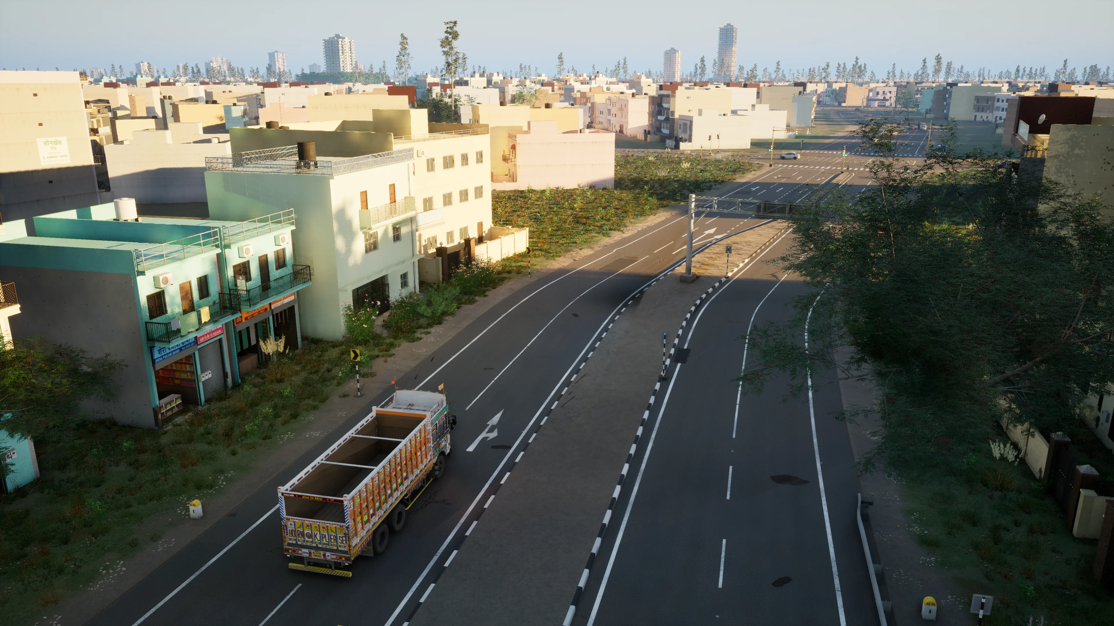 High view of a town road past teal shop-houses, a painted truck heading for the junction and towers on the horizon, at golden hour